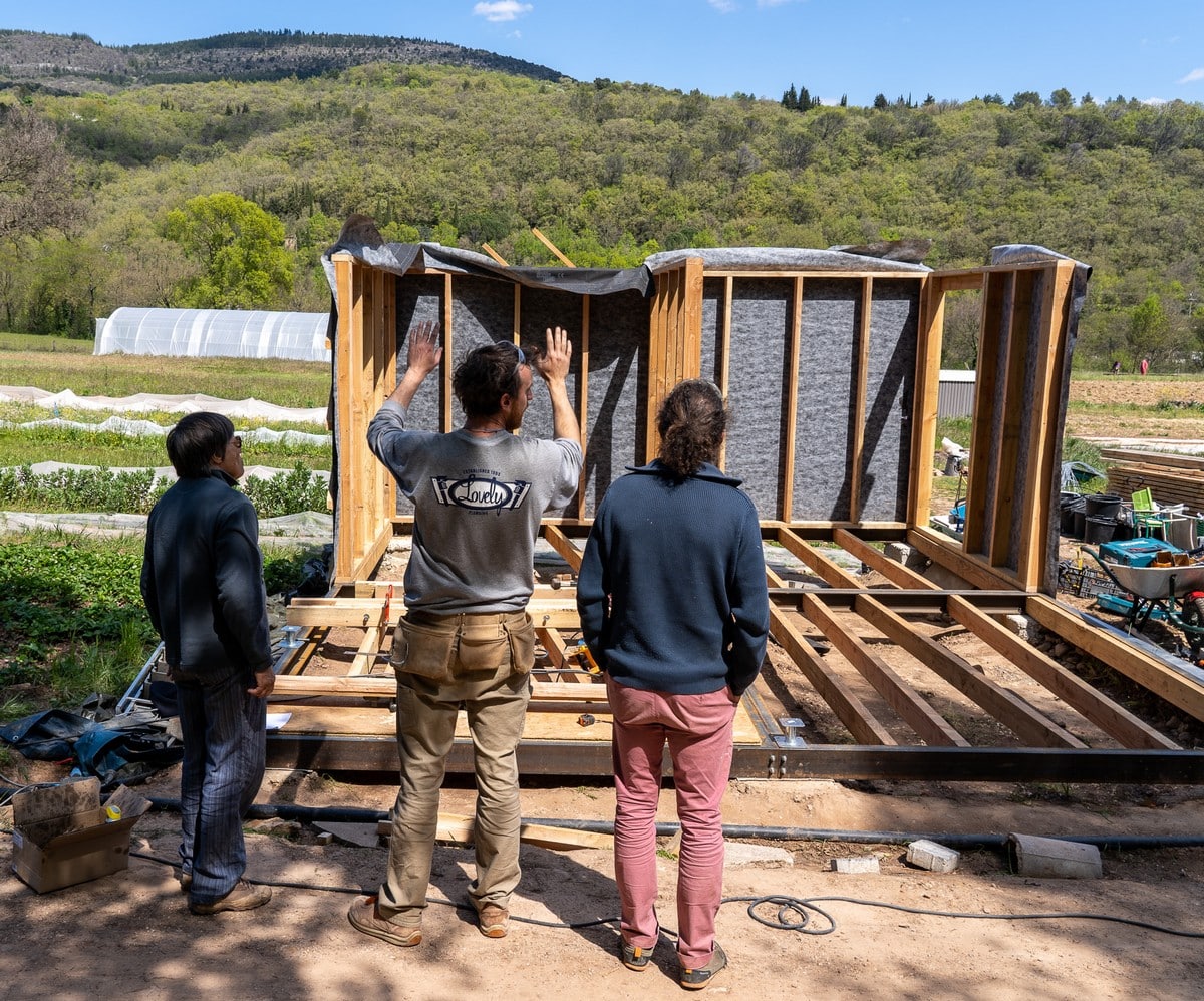 © Bastien Defives. Pose ossatures murs (extérieurs et intérieurs) et ossatures toiture. Projet BatiAlim. Formation à l'autoconstruction agricole donnée par 3PCo. Sur la parcelle du Jardin de Campeyrou. Avec l'aide du collectif Résilience alimentaire de Lodève. Campeyrou, Lodève. Hérault.